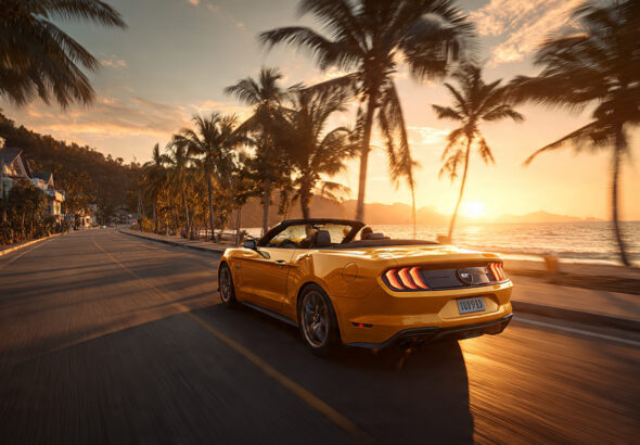 Желтый кабриолет Ford Mustang едет по живописной трассе вдоль моря в Паттайе на закате